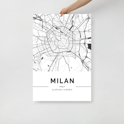 A hand holds the FN Prints "Milan City Map" poster, showcasing a sophisticated black and white street map of Milan, Italy. The coordinates 45.467729, 9.188030 are elegantly printed below, making it a striking piece of urban design wall art.