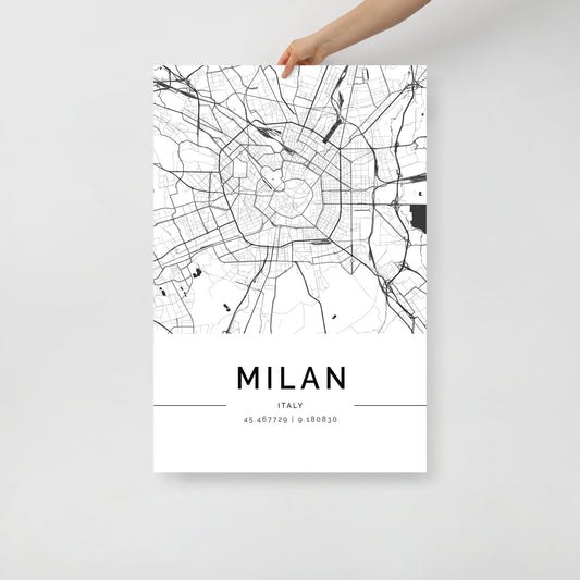 A hand holds the FN Prints "Milan City Map" poster, showcasing a sophisticated black and white street map of Milan, Italy. The coordinates 45.467729, 9.188030 are elegantly printed below, making it a striking piece of urban design wall art.