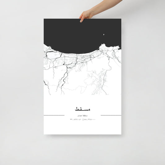 A hand holding a black and white minimalist city map poster of Muscat, with distinct outlines of streets and districts against a white background.