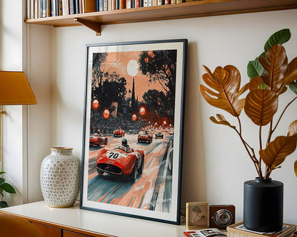 The FN Prints "Retro Grand Prix" framed poster, featuring vintage racing cars under a large moon, is displayed on a shelf with a decorative vase, camera, books, and greenery provided by a nearby plant.