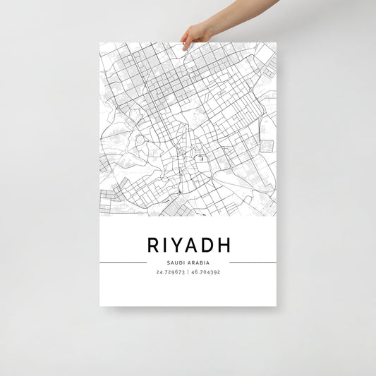 A person holds a Riyadh City Map by FN Prints, featuring an urban tapestry with detailed grid lines and street information in black and white. The city's name and coordinates, 24.7136° N, 46.6753° E, are elegantly displayed at the bottom to complete the striking poster.