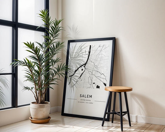 A framed FN Prints Salem City Map rests against a wall in a bright room, adding minimalist flair. A potted plant and wooden stool enhance the light wood floor, crafting an inviting space for city art lovers.