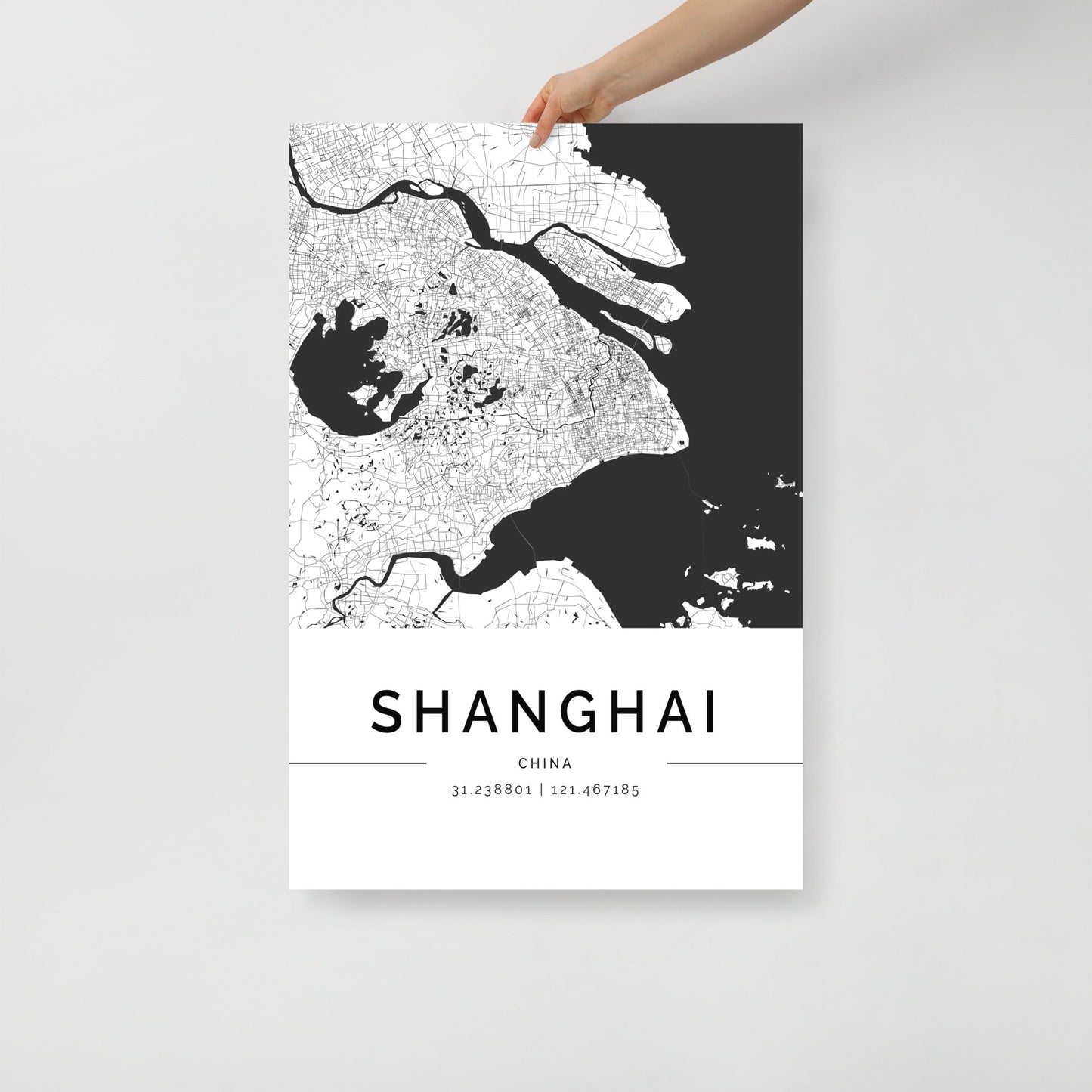 A hand holds a striking wall art print from FN Prints—a must-have for map lovers—featuring the Shanghai Map. The detailed city map beautifully renders intricate street patterns and waterways, with "Shanghai" in bold at the bottom alongside its geographic coordinates.