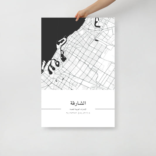 A hand holding a black and white map poster of Sharjah city, with distinct lines representing streets and boundaries on a white background.