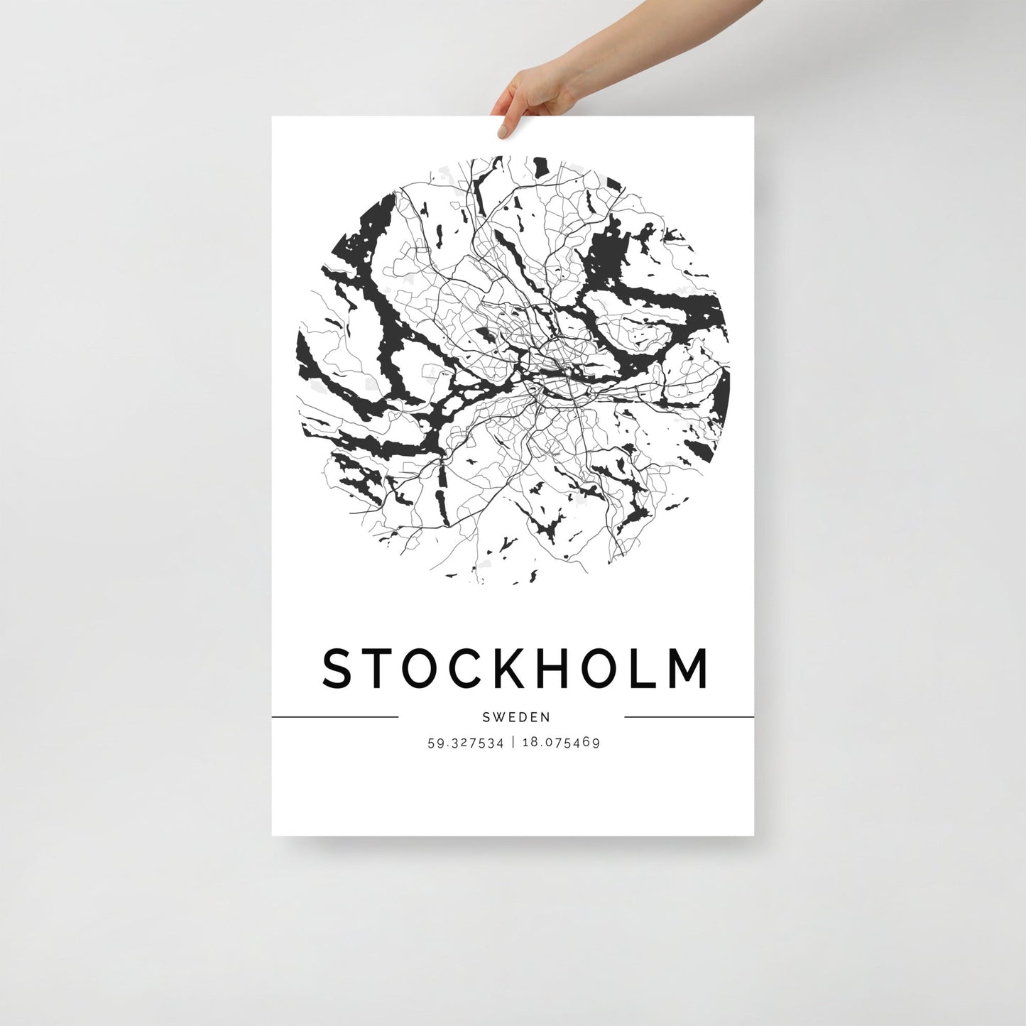 A person holds an eye-catching Stockholm City Map by FN Prints, a black and white poster with a circular design. It's ideal wall art, intricately detailed with geographic coordinates: 59.327354 | 18.075469, displayed below the prominent "STOCKHOLM" text.