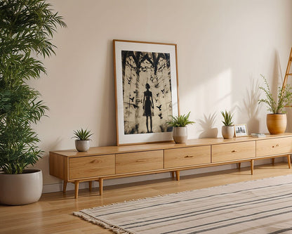 A minimalist living room showcases a long wooden console adorned with potted plants, enhanced by dramatic lighting and a framed art piece titled "The Birds" by FN Prints, depicting a silhouetted figure and birds. A large plant occupies the floor space, while a striped rug adds texture to the wooden flooring.