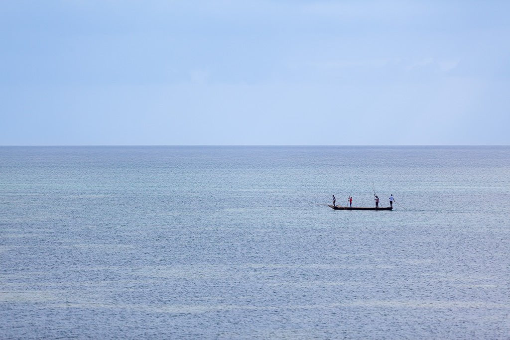 Minimalist fine art photography of a small fishing boat with three people on a calm, misty blue sea in Vietnam with no visible horizon.
