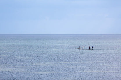 Minimalist fine art photography of a small fishing boat with three people on a calm, misty blue sea in Vietnam with no visible horizon.