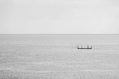 Minimalist fine art photography of a small fishing boat with three people on a calm, misty blue sea in Vietnam with no visible horizon.