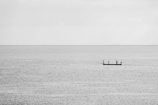 Minimalist fine art photography of a small fishing boat with three people on a calm, misty blue sea in Vietnam with no visible horizon.