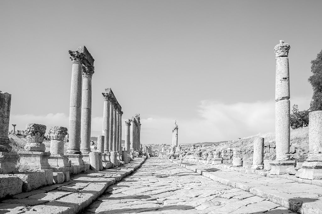 Black and white fine art photography of the Cardo Maximus in Jerash, Jordan, featuring a long row of ancient Roman columns and a stone-paved walkway.