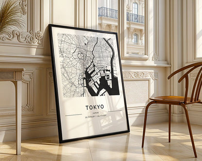 The FN Prints Tokyo City Map poster, framed and in black and white on premium paper, leans against the wall on a wooden floor beside a chair. The bright room features large windows and ornate architectural details.