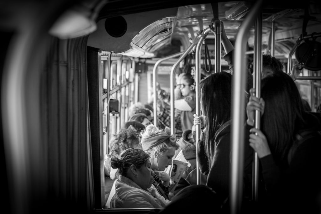 Tram Tales by FN Prints beautifully captures the urban sophistication of San Francisco street life with a black and white photo on a crowded bus. Passengers engrossed in their own activities, whether gazing at their phones or looking out the window, embody the essence of fine art photography amidst handrails and seats.