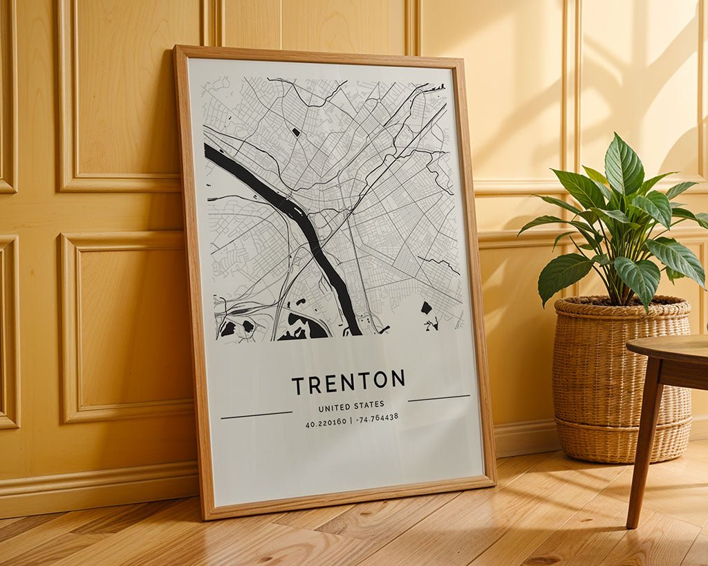 The FN Prints Trenton City Map, featuring geographic coordinates, is displayed against a light yellow paneled wall. This museum-quality print exemplifies stunning city wall art. A green plant in a woven basket is placed on the wooden floor to the right.