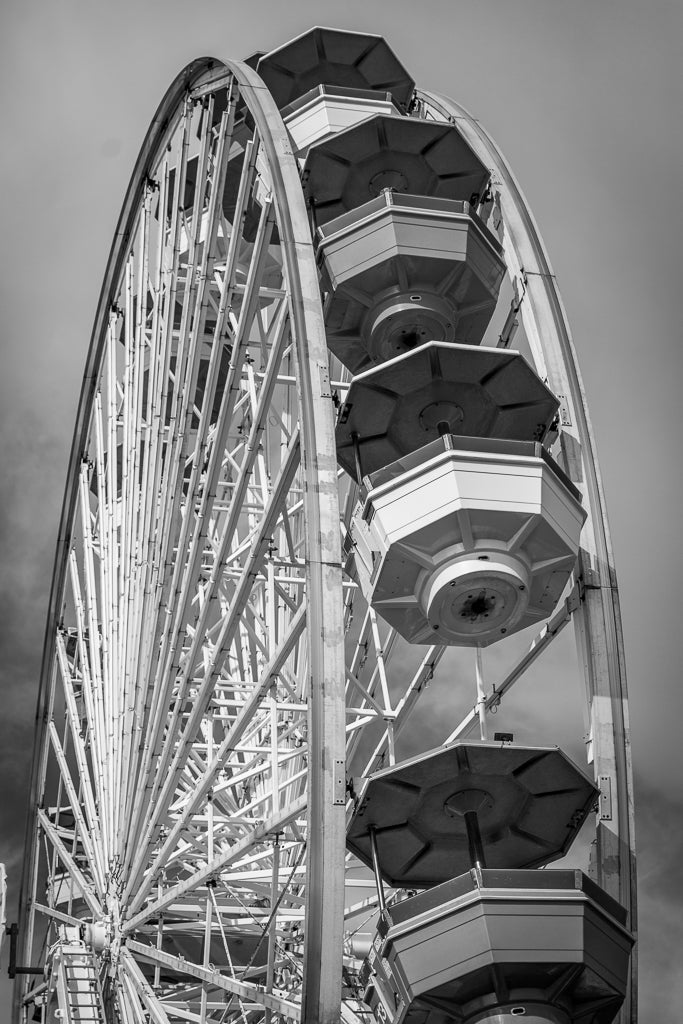 A close-up black and white photograph titled "Ferris Wheel" by FN Prints, showcasing the towering structure and attached gondolas of a Ferris wheel. The partly cloudy sky in the background enhances its vintage charm, making it perfect for Ferris wheel photography enthusiasts or as classic wall art.