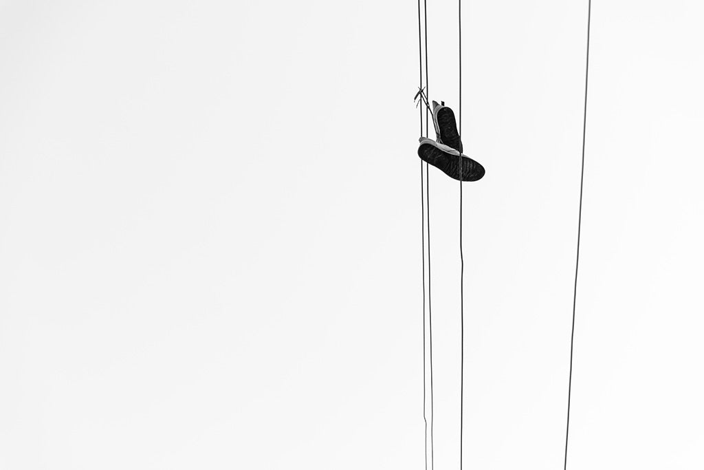 Minimalist black and white fine art photography of a pair of sneakers hanging from power lines against a white sky in Amman, Jordan.