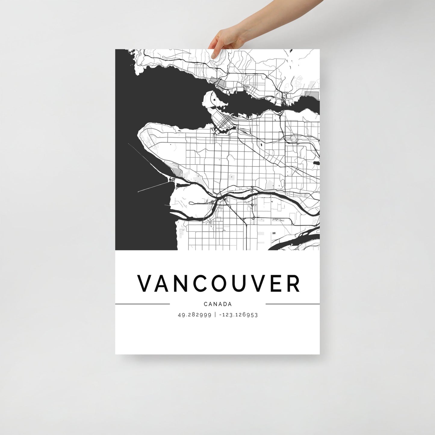 A hand holds a beautifully crafted black and white Vancouver City Map by FN Prints, showcasing intricate streets and geographical features. The bottom of this stunning wall art includes the city's name along with its precise coordinates, 49.282999, -123.126953.