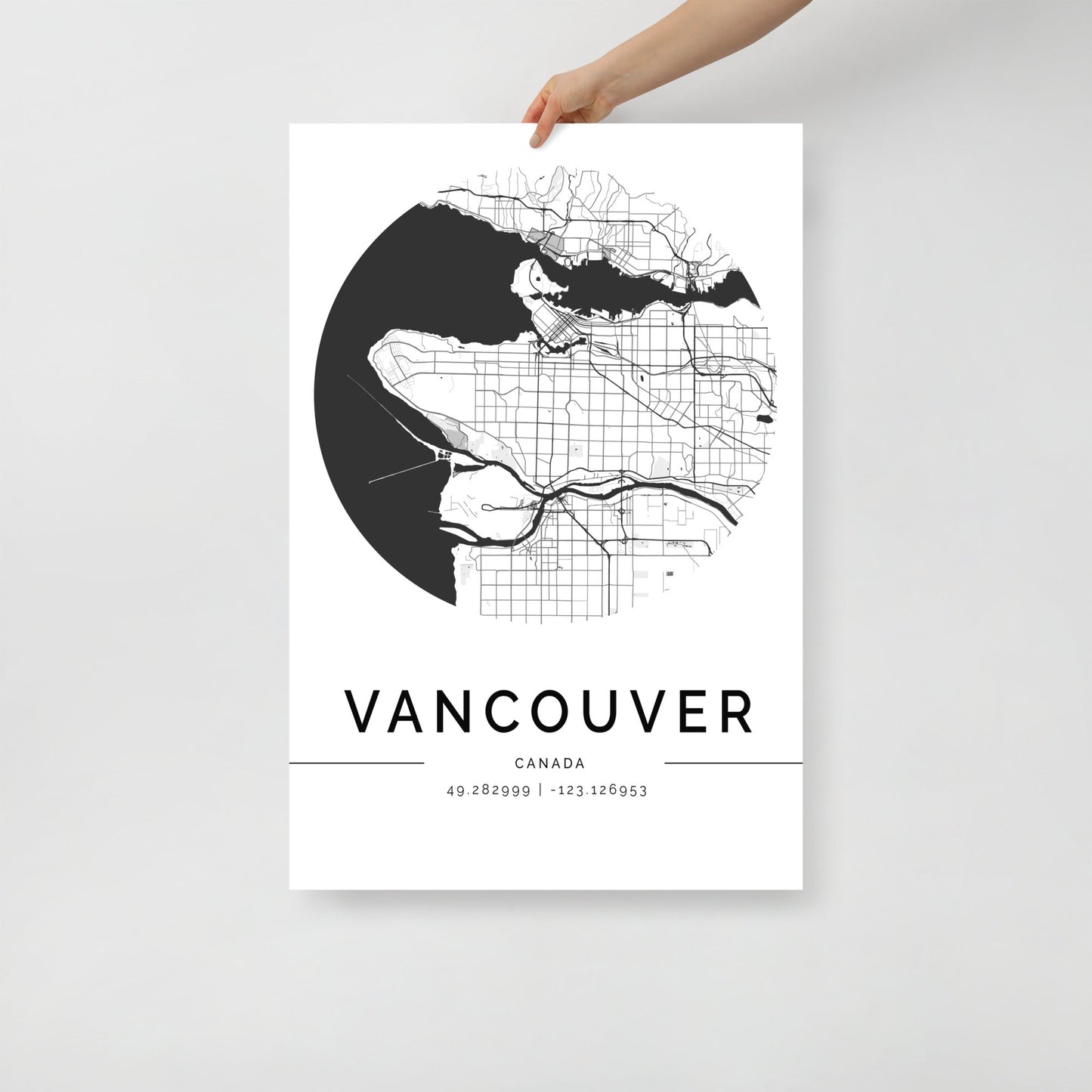 A person holds the FN Prints Vancouver City Map, a circular black and white map poster displaying intricate street patterns. Ideal as wall art, this piece highlights "Vancouver Canada" along with the coordinates "49.282999, -123.126953" at the bottom.