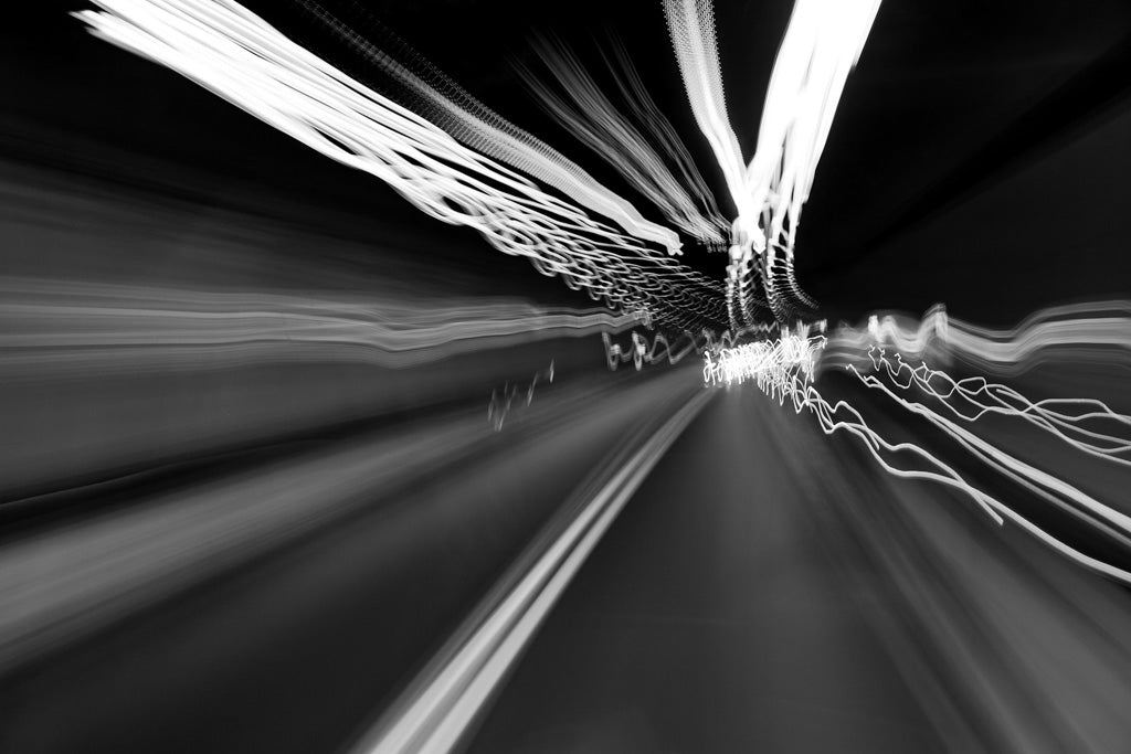 Introducing "Warp Speed" by FN Prints: A stunning black-and-white composition that captures abstract photography with dynamic light trails streaking across the frame. The curved light patterns convey a sense of motion, reminiscent of a long-exposure capture in an urban landscape or tunnel.